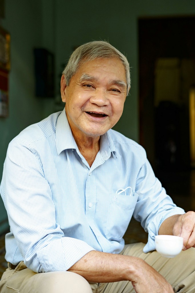 A smiling older man holding a cup of tea at home